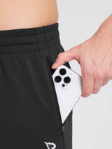 Man's hand placing a smartphone into a zippered pocket of black reflective fleece jogger pants. #color_Black