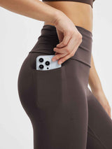 Woman's hand places a smartphone into the deep side pocket of dark gray yoga flared pants. #Color_Seal Brown