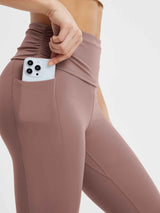 Brown yoga flared pants with fold-over waistband and side pocket holding a smartphone. #Color_Brown