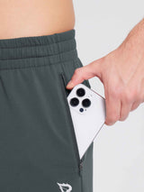 Man placing phone into zippered pocket of men's reflective fleece jogger pants in dark gray. #color_Dark Gray
