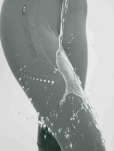 Grey fleece leggings show water beading off, featuring zippered pocket and reflective dots. Waterproof cycling wear.