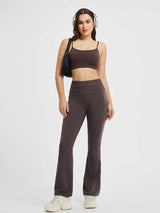 Woman in brown yoga flared pants, fold-over waistband, matching crop top, white sneakers, headphones, and black bag. #Color_Seal Brown