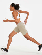 Woman in light khaki 7" running shorts with built-in liner and white sports bra in motion. #color_Khaki