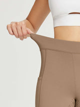 Woman pulling the waistband of brown fleece-lined breeches, showing stretch and pocket detail. #color_Brown