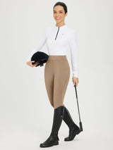 Tan full-seat fleece silicone breeches on a woman, holding helmet and whip. Horse riding attire. #color_Brown