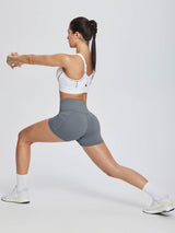 Woman in grey high-waisted compression biker shorts stretching on a white background. #color_Dark Gray