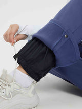 Woman adjusting drawstring on blue heavyweight fleece ski pants with black inner lining and white sneakers. #color_Navy Blue