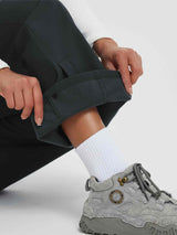 Woman's hand unrolling the cuff of dark green fleece-lined outdoor pants, revealing the soft thermal interior. #color_Black