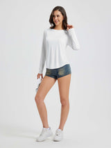 Woman wearing a white long sleeve running shirt and denim shorts, holding white headphones. #color_White