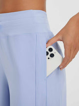 Woman placing a smartphone into the deep side pocket of light blue UPF 50+ running capris. #color_Light Blue