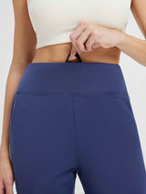 Woman pulling the drawstring on the flat waist of navy blue fleece-lined running joggers. #color_Blue/White