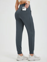 Woman wearing dark grey fleece-lined joggers with a phone in a zippered back pocket. #color_Charcoal Gray