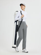 Woman in grey tapered pants and white long-sleeve top carrying a white golf bag. #color_Dark Gray