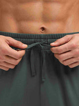 Man adjusting drawstring on dark gray fleece running pants with dual pockets. #color_Army Green