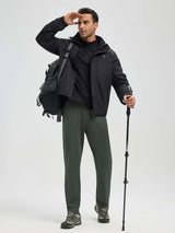 Man in dark green tapered pants and black jacket with backpack and hiking pole, looking into distance. #color_Army Green