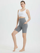 Woman wearing grey 8" super high-waisted biker shorts with pockets, paired with a white sports bra. #color_Dark Gray