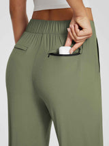 Woman's olive green high-waist tapered yoga pants with zippered pocket holding AirPods case #color_Army Green