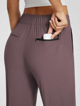 Woman placing white earbuds case into a zippered pocket on mauve tapered yoga pants. #color_Dark Brown