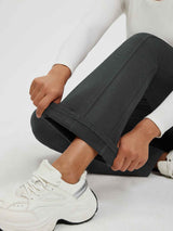 Woman adjusting hem of dark gray floral fleece yoga pants, wearing white sneakers.