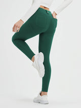 Woman wearing dark green fleece-lined high-waisted leggings with multiple pockets and white sneakers. #color_Green