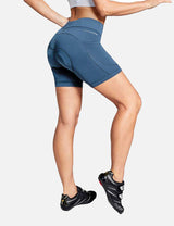 Woman in blue V-waist cycling shorts with padded inserts and side pockets, wearing cycling shoes. #color_Navy Blue