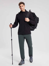 Man in black fleece joggers, black jacket, and hiking boots holding a trekking pole with a backpack. #color_Dark Gray