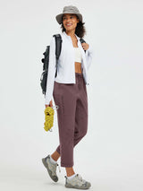 Woman wearing dark plum straight-leg outdoor hiking pants with a white zip-up jacket and a gray bucket hat. #color_Dark Brown