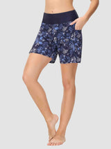 Woman wearing navy blue board shorts with a white and blue tropical leaf print and a navy blue waistband. #color_Print 1
