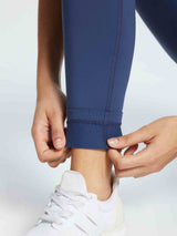 Close-up of navy blue 3/4 thermal ski leggings being adjusted at the ankle, paired with a white sneaker. #color_Navy Blue