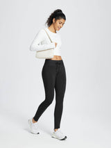 Woman in black water-resistant 3/4 thermal ski leggings with white top and bag #color_Black