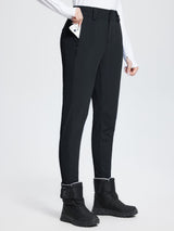 Black stretch knit slim-fit ski pants with zippered pocket, worn by a woman with winter boots. #color_Black