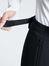Woman adjusting velcro waistband on black slim-fit ski pants with zipper detail. #color_Black