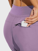 Woman's hand puts white earbuds in zippered pocket of lavender women's tall high-waisted hiking joggers. #color_Purple