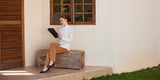 Woman sitting outdoors wearing tan fleece lined pants and white blouse while reading on a clipboard