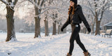 A woman wearing a black puffer jacket and fleece lined leggings walking briskly along a snowy, tree-lined path.