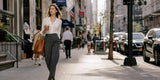 Woman in gray dress pants walking through a city with coffee and tote bag