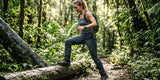 Woman hiker stepping over a fallen log on a lush forest trail