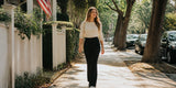 A woman walks along a tree-lined sidewalk wearing black straight-leg pants and a cream sweater