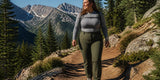 A woman in a gray long-sleeve top and olive hiking pants walks along a rocky mountain trail with a backpack
