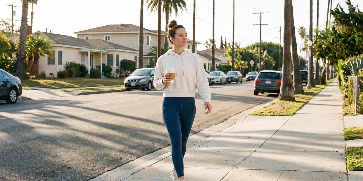 Woman in a white sweatshirt and blue leggings walking along a sunny sidewalk