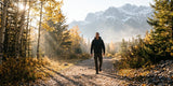 Hiker walking along a sunlit forest trail with mountains in the background