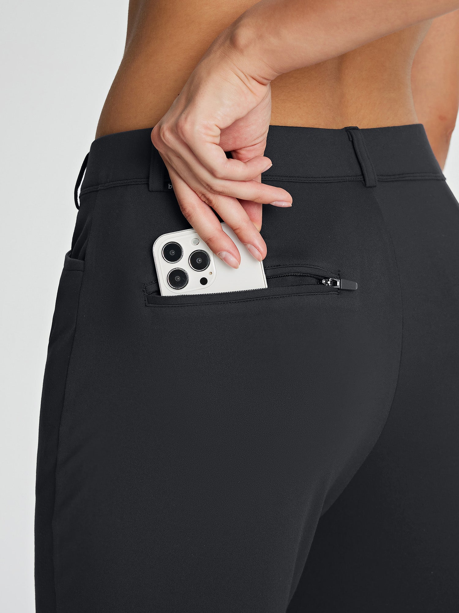 Black women's fleece-lined golf pants with a phone being placed in a zippered back pocket. #color_Black