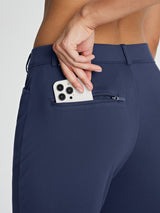 Navy blue women's fleece-lined golf pants with hand placing phone in zippered back pocket.