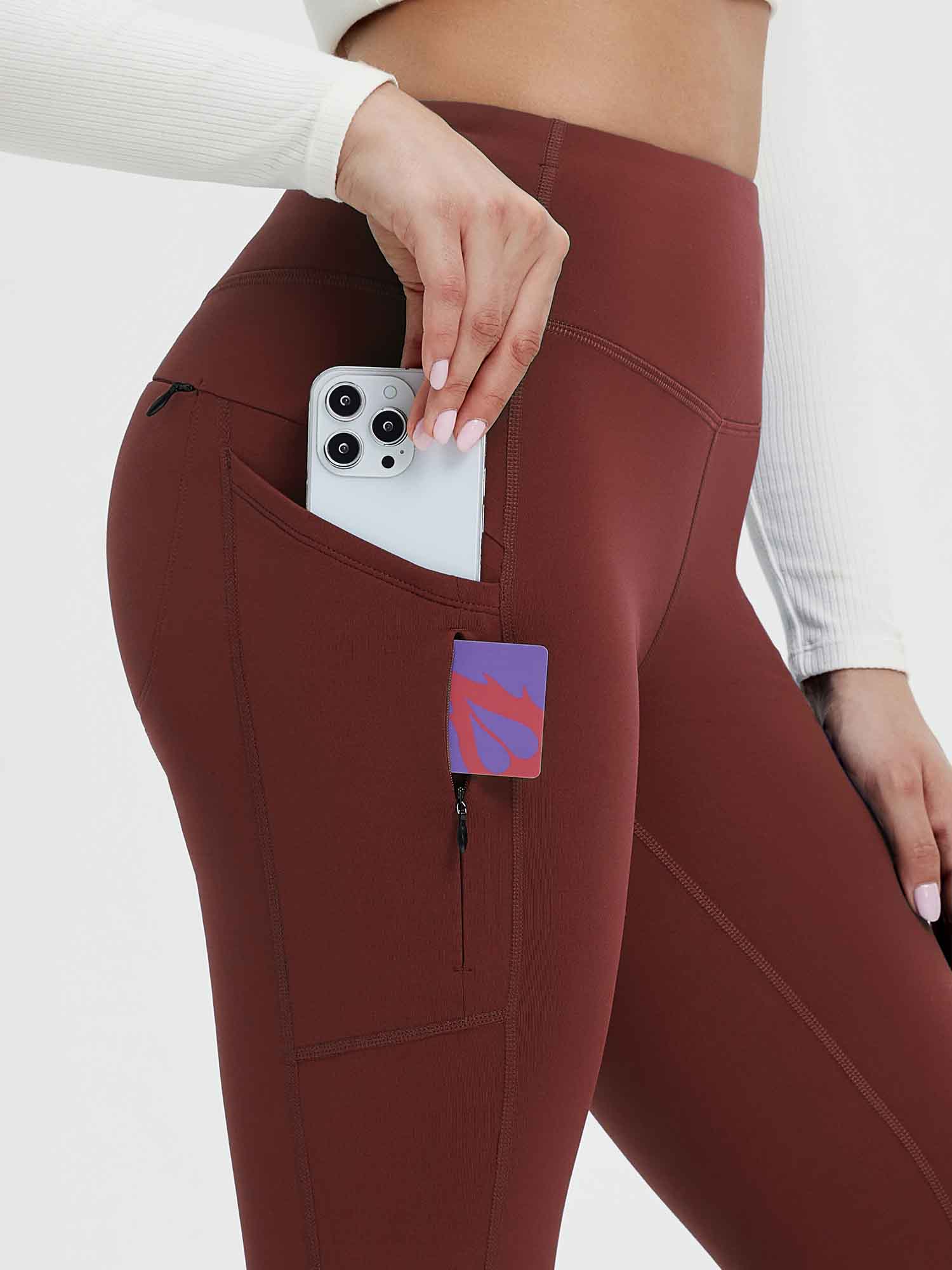 Woman's hand placing phone into side pocket of wine red fleece-lined yoga leggings with zippered pocket. #color_Wine Red