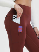 Woman's hand placing phone into side pocket of wine red fleece-lined yoga leggings with zippered pocket. #color_Wine Red