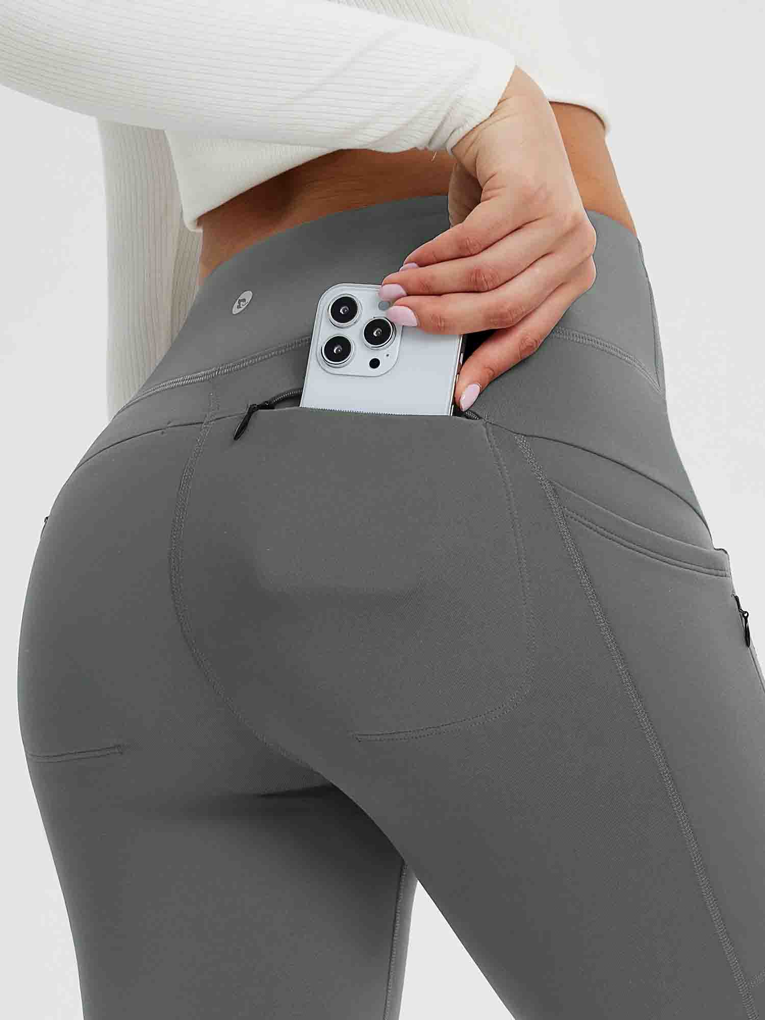 25" grey fleece-lined yoga leggings with side pockets and a zippered pocket holding a smartphone. #color_Dark Gray