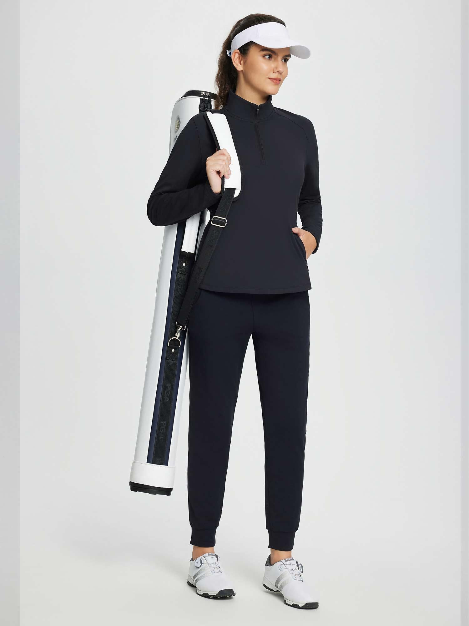 Woman wearing a black half-zip fleece pullover golf top and navy pants, carrying a white golf bag. #color_Black