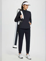 Woman wearing a black half-zip fleece pullover golf top and navy pants, carrying a white golf bag. #color_Black