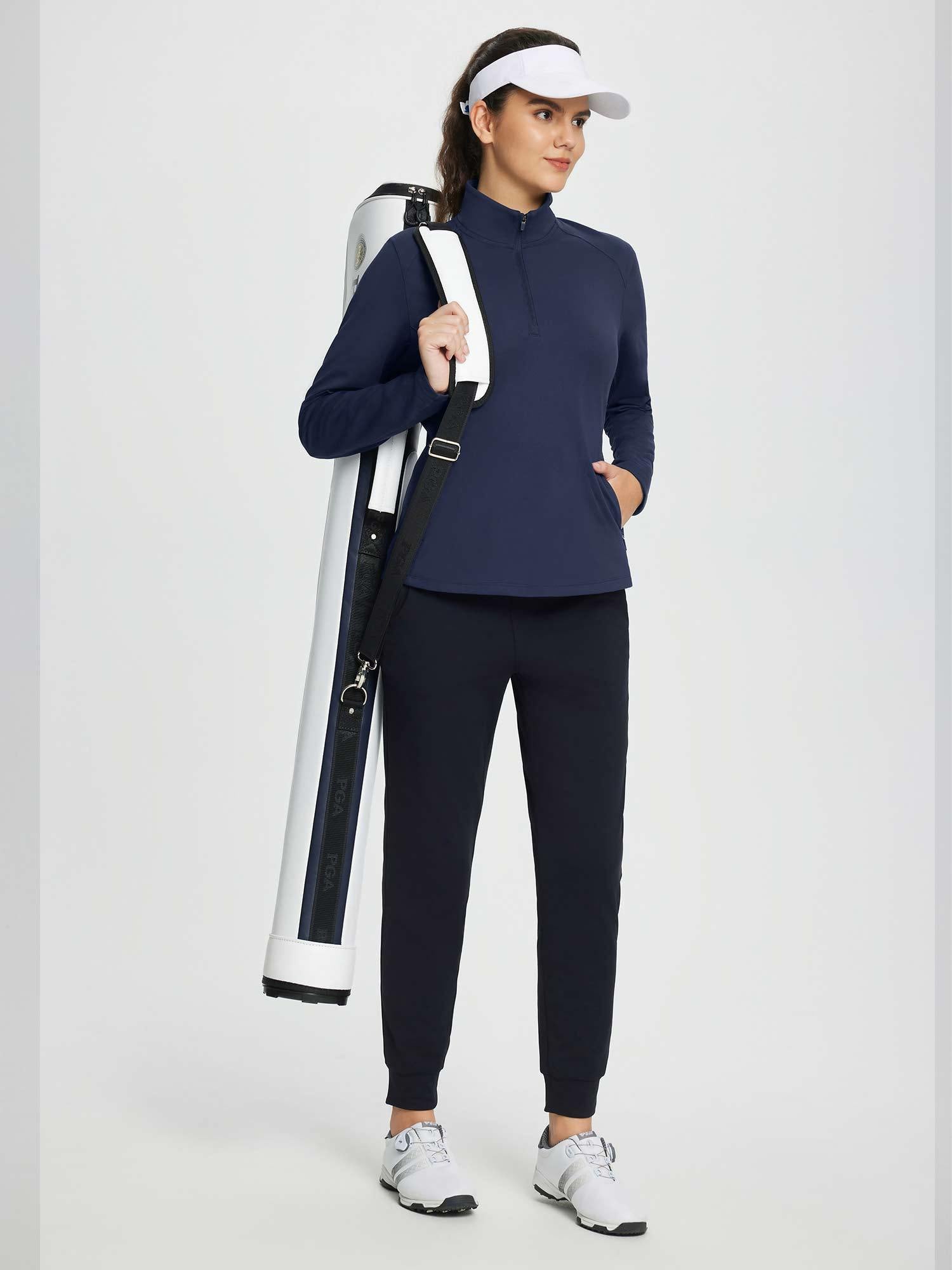 Women's navy blue half-zip fleece pullover golf top with black joggers and white visor, carrying a PGA golf bag.