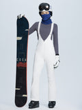 Woman in white ski bib pants and grey long-sleeve top holding a snowboard with 'COSA' branding. #color_White